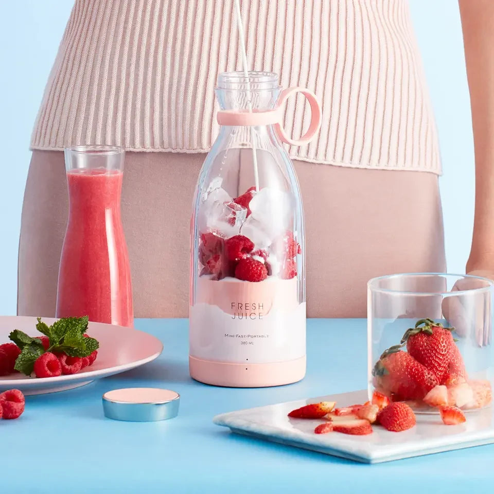 Portable pink blender with strawberries, ice, and fresh juice on a kitchen counter